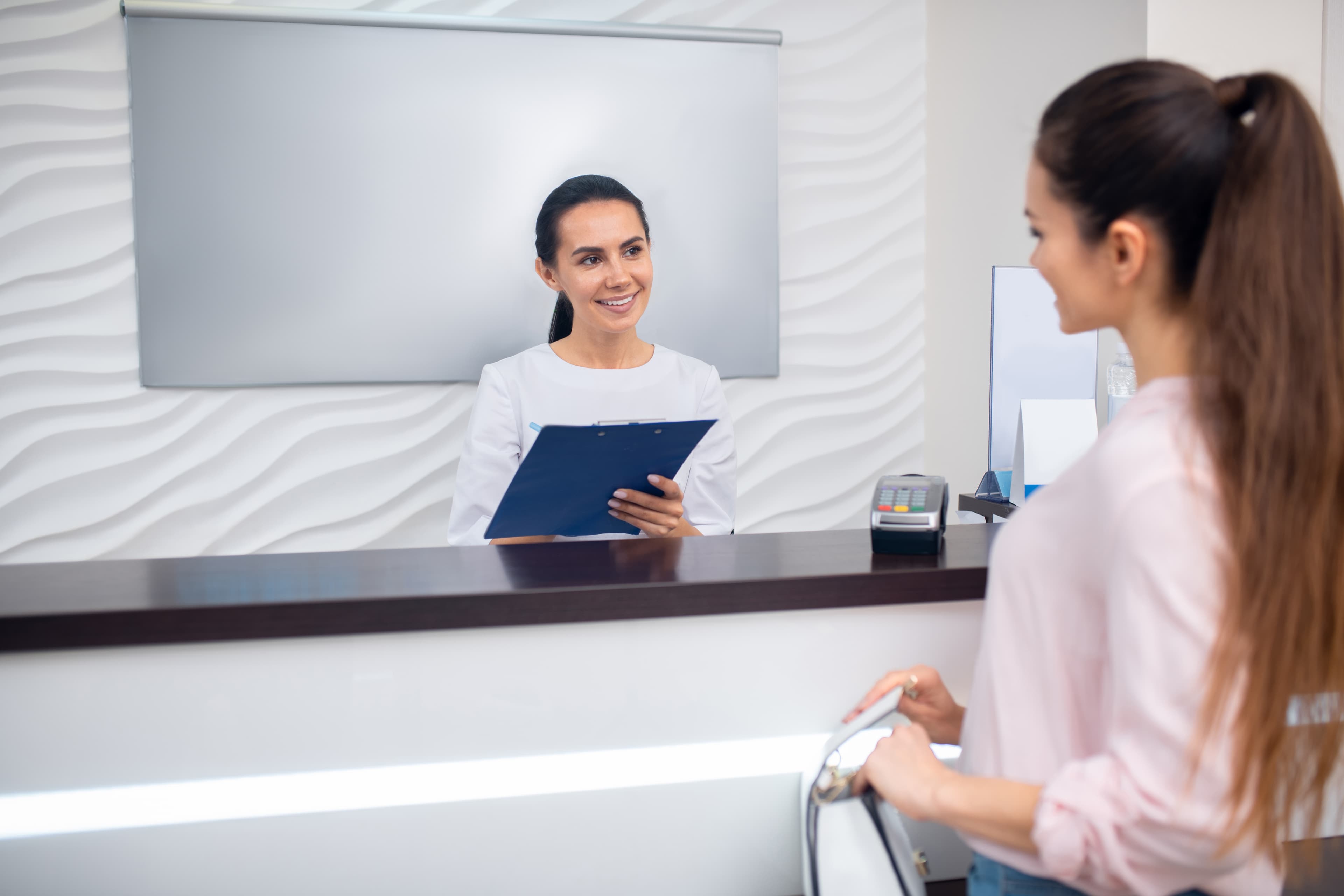 Friendly clinic receptionist helping a parent at the front desk